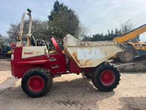 Red and white Thwaites Mach 591 Site Dumper with raised tipping bed in an outdoor yard, with JCB equipment in the background