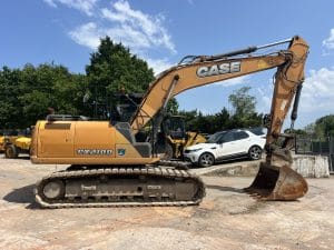 Case CX210D excavator with a large bucket, parked on a construction site with machinery in the background.