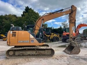 Orange CX300 excavator with a large bucket, parked on a construction site with machinery in the background.