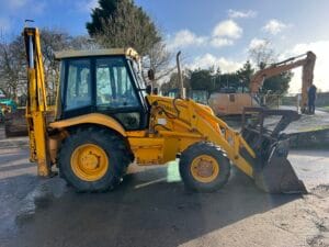 Yellow backhoe loader with a front bucket and rear excavator arm on a construction site.